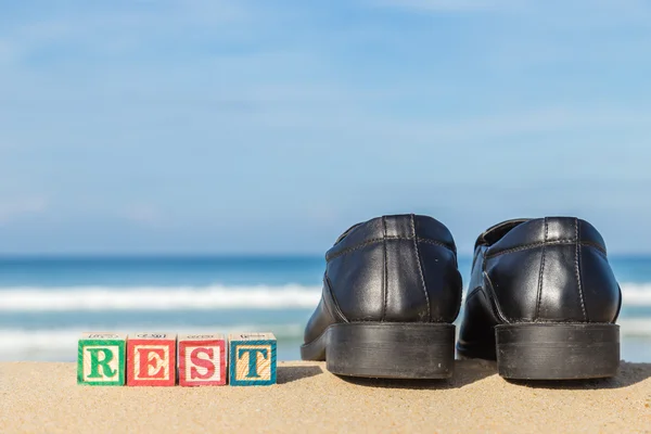 Word REST in colorful alphabet blocks and black shoe on tropical