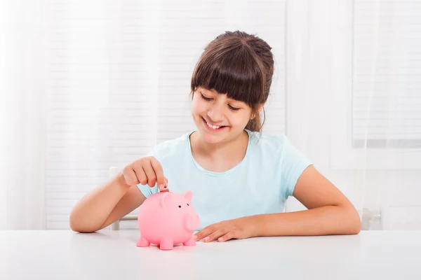 Girl putting coin into piggy bank.
