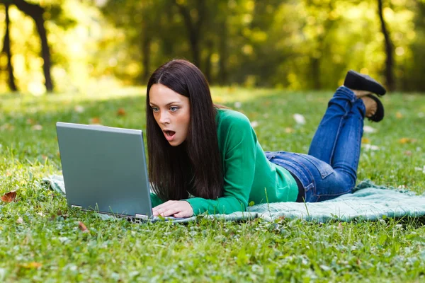 Woman is using her laptop while lying down in nature
