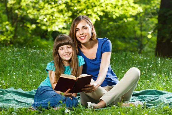 Girl and mother reading book outdoors