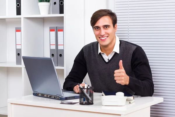 Businessman sitting in his office and showing thumb up