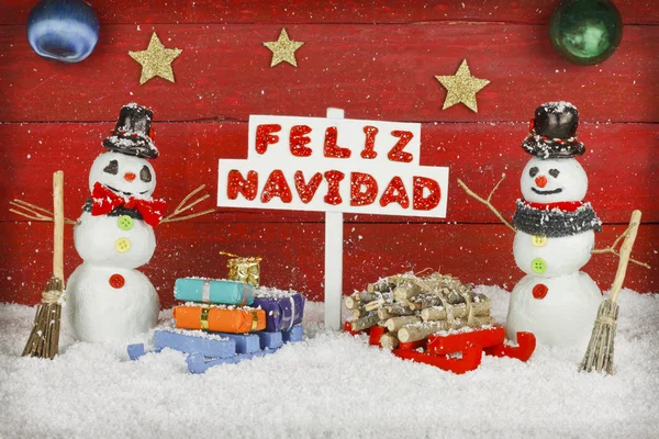 Two snowmen holding a sign with the words Merry Christmas written on spanish