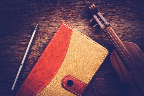 Violin and notebook with pen on grunge dark wood background