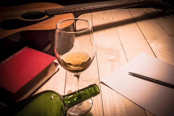 Guitar with Red Book and Wine on a wooden table.