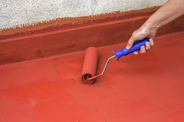 Hand painting a red floor with a paint roller
