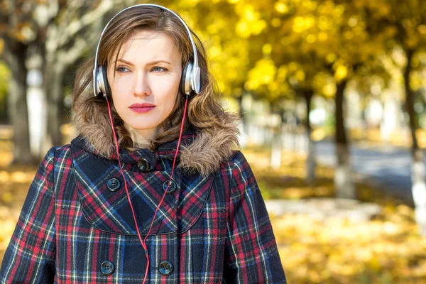 Beautiful autumn woman listening to music in autumn golden park