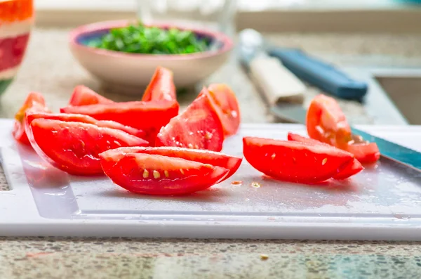 Fresh sliced tomato pieces, in the background a small bowl of freshly chopped chives. Tomato pieces