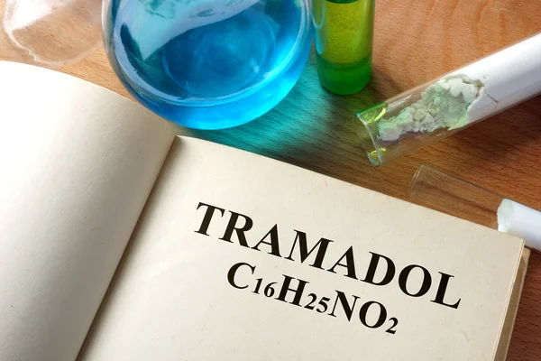 Book with tramadol and test tubes on a table.