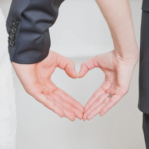 Wedding couple showing shape of heart from their hands.