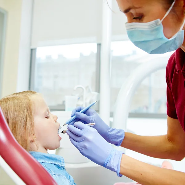 Pediatric dentist examining little girls teeth in the dentists chair