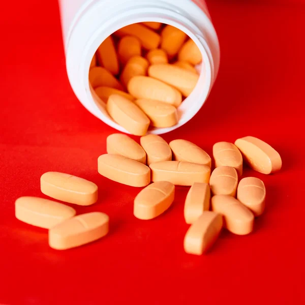 Pills spilling out of pill bottle on red. Top view with copy space.