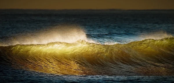 Golden and blue waves breaking at sunset