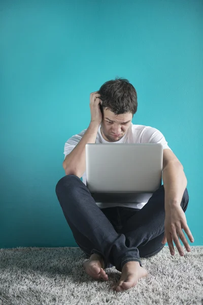 Young man in t-shirt sitting at home, working on laptop computer