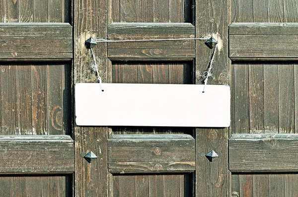 Blank white sign hanging with tattered rope on the old brown wooden wall with metal rivets -  background in retro tones