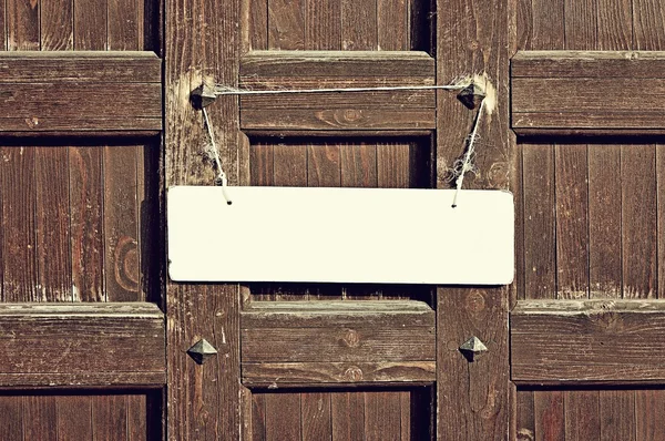 Blank white sign hanging with old rope on the weathered brown wooden wall with metal rivets - retro tones background