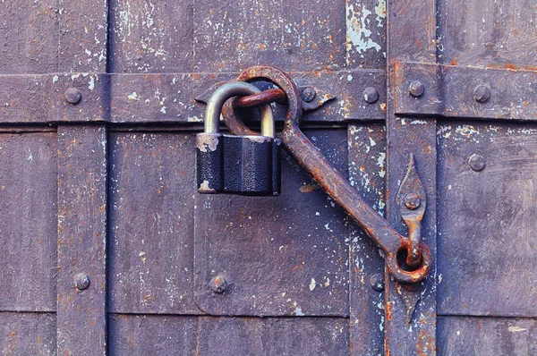 Industrial background - iron old padlock keeping the aged door heck at the rusty riveted door.