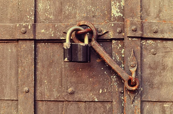 Grunge background - iron black padlock keeping the old door heck at the iron forged aged riveted door.