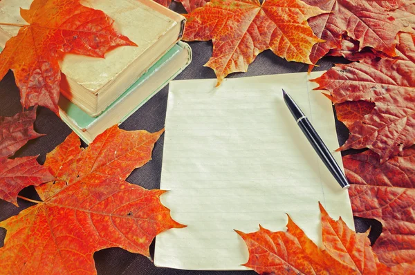 Old books with yellowed sheet and old ink pen near autumn dry maple leaves - autumn vintage still life