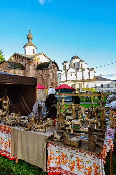 Fair in traditional Russian style at Yaroslav Courtyard - people in Slavic clothes and various wooden handicrafts on the counter. Veliky Novgorod, Russia