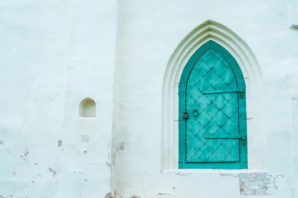 Turquoise metal forged door with arcade on the white stone wall of the medieval Slavic church of Fedor Stratilates in Veliky Novgorod, Russia.