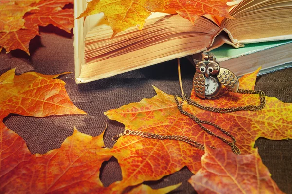 Old books with clock near  maple leaves - autumn still life
