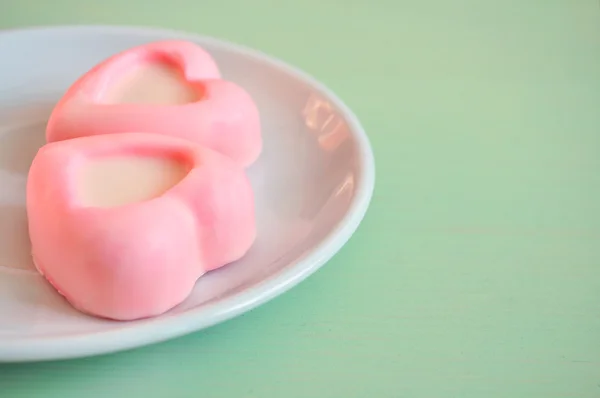 Two heart-shaped pink souffle cakes lying on the white plate on the green wooden table. Selective soft focus on the cake. Pastel processing.