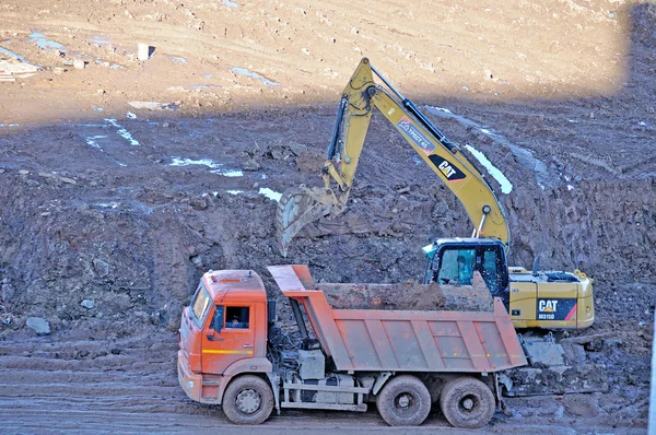 Excavator loads the truck body with large clods of earth during construction works at the building site