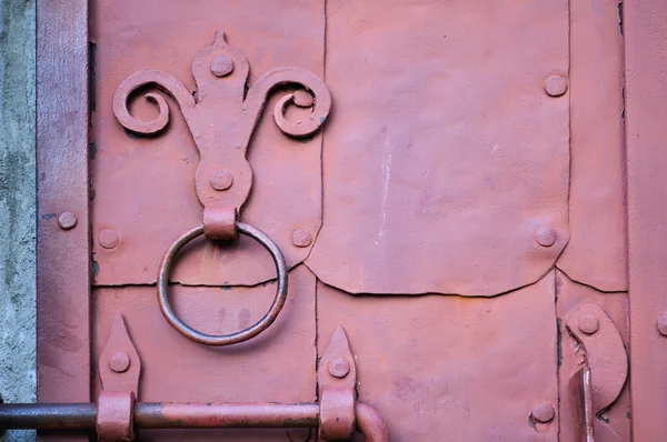 Industrial textured background - Old dark pink door with rivets and aged metal door handle in the form of stylized lily.
