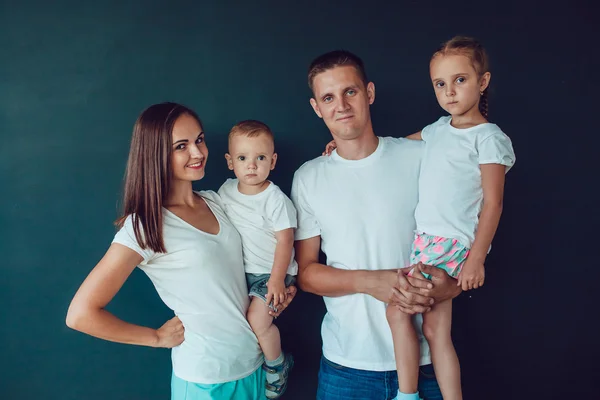 Young family of four standing in white shirt over black background