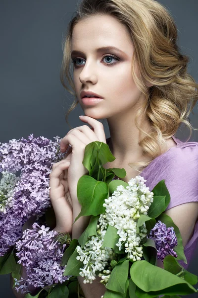 Beautiful girl in a purple dress and a bouquet of lilacs. The model is in an image of spring.
