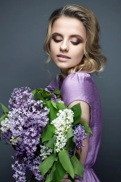 Beautiful girl in a purple dress and a bouquet of lilacs. The model is in an image of spring.