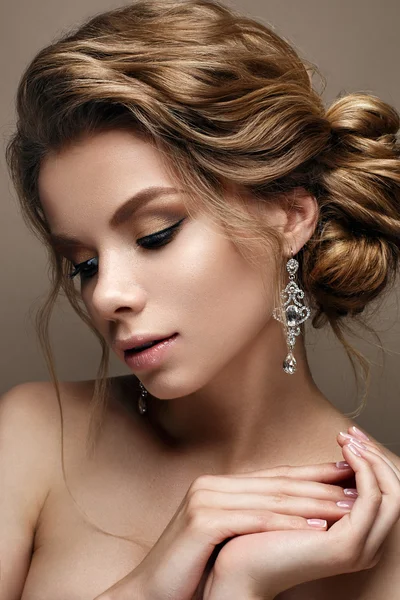 Beautiful girl in the image of a bride with bright earrings. Model with a gentle makeup in beige tones.