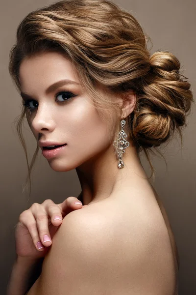 Beautiful girl in the image of a bride with bright earrings. Model with a gentle makeup in beige tones.
