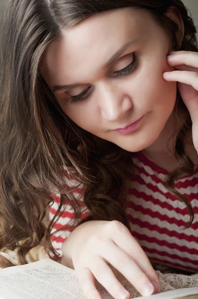 Beautiful girl reading a book lying on the bed in the evening