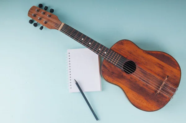 Little guitar and blank notebook with pencil on the azure surfac