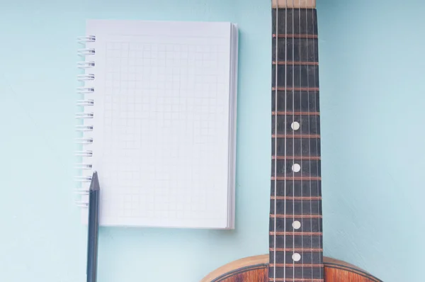 Little guitar and blank notebook with pencil on the azure surfac