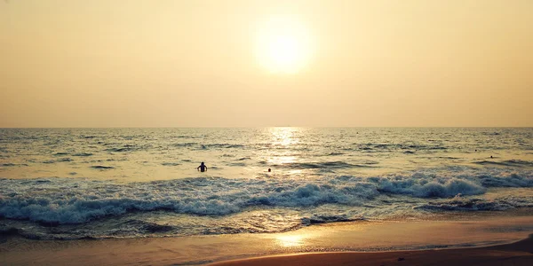 A few tourists on the tropical ocean beach - retro effect. Sunset in Varkala, Kerala, India.