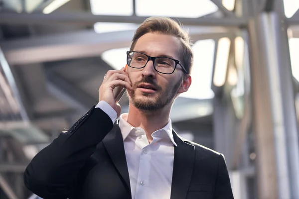 Portrait of handsome businessman in suit and eyeglasses speaking on the phone in airport