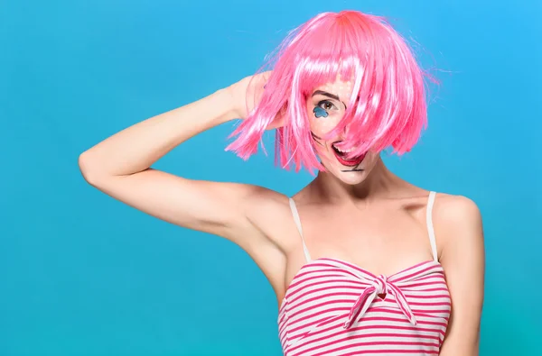 Beauty head shot. Young woman with creative pop art make up and pink wig looking at the camera on blue background