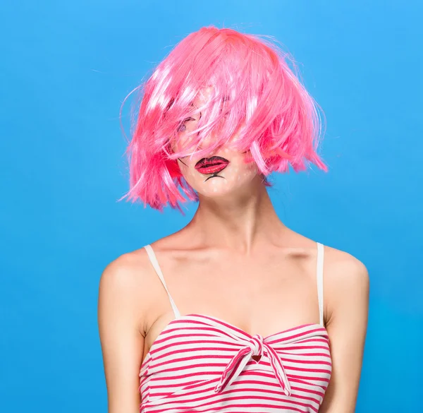 Beauty head shot. Young woman with creative pop art make up and pink wig looking at the camera on blue background