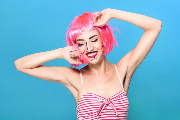 Beauty head shot. Young woman with creative pop art make up and pink wig looking at the camera on blue background