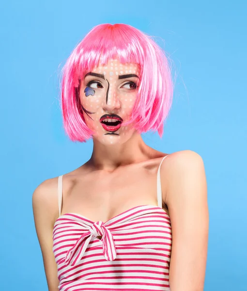 Beauty head shot. Surprised Young woman with creative pop art make up and pink wig looking at the camera on blue background