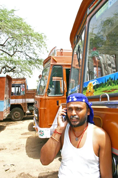 Kerala,India - July 13, 2004: Indian truck driver talking on his mobile phone with trucks parked on his back.