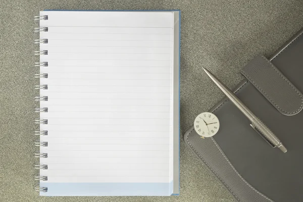 Notebook, pen, and clock with part of closed business notebook
