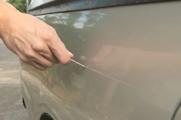 Male hand scratching a car by using silver key