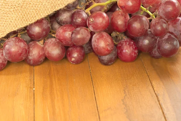 Part of branch of red grape pouring out of old agriculture sack on top of wooden table with hugh negative space for usage