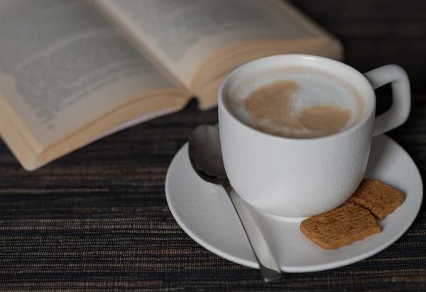 Morning coffee with milk foam , cookie and book