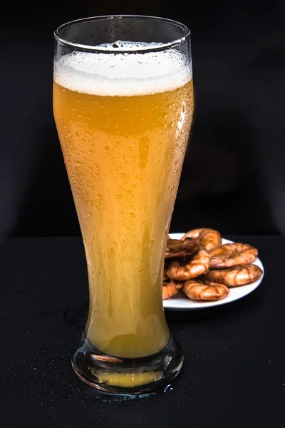 Unfiltered cold foamy beer in a tall glass with a snack of fried shrimp