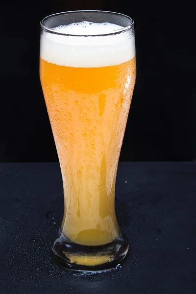 Unfiltered cold foamy beer in a glass on the black background. холодное нефильтрованное пенистое пиво в бокале на черном фоне.