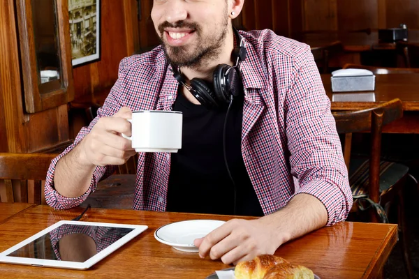 Man drinking coffee with headphones and digital tablet.